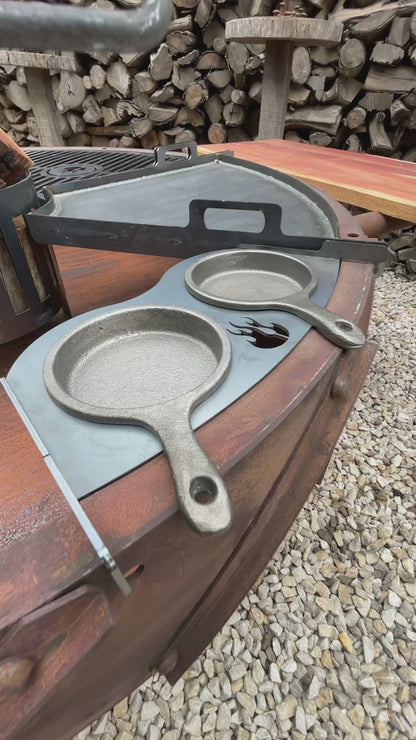 Odin PRO cart grill in rust: a quarter of the grate lifts out, firewood loads into the ember basket, and the crank raises the cooking surface